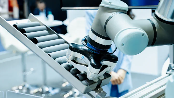Braț robotic deasupra unei benzi cu role, la un stand de automatizări